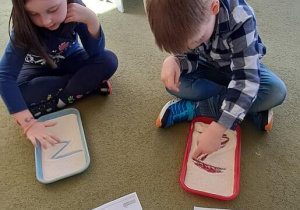 Hania i Mateusz rysują litery "Z" na tackach z kaszą manną do piosenki "Zuzanna"