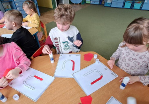 Hania, Gabryś, Misia wyklejają wzory litery "U" czerwoną wydzieranką