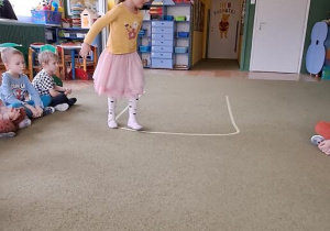 Klara spaceruje po wyklejonej taśmą na dywanie literze "U"