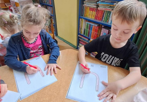 Marysia i Tymek piszą litery "U" na kartkach czerwonymi kredkami w rytmie piosenki "Ula"