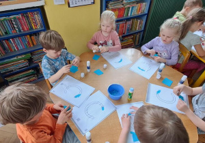 Dzieci przy niebieskim stole wyklejają niebieską wydzieranką wzory litery "C"