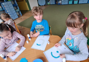 Hania, Gabryś i Misia wyklejają niebieską wydzieranką wzory litery "C"