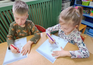 Mateusz i Klara piszą litery "Ł" kredkami na kartkach do piosenki "Łukasz"