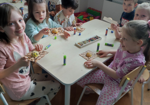 Dzieci siedzą przy stoliku, tworzą własne mrowiska z przygotowanych materiałów