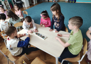 Dzieci siedzą przy stoliku, malują pastelami przygotowane materiały do pracy