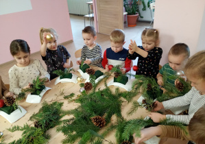 Dzieci z entuzjazmem pracują przy stolikach, tworząc wyjątkowe świąteczne stroiki.