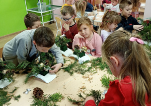 Dzieci z zapałem tworzą świąteczne stroiki, starannie pracując przy stolikach.