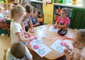 Dzieci przy żółtym stoliku wykonują pracę plastyczną "Rower"