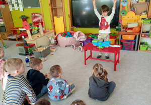 Chłopiec trzyma w ręku dwa przedmioty, dzieci próbują określić, który jest lżejszy, który cięższy