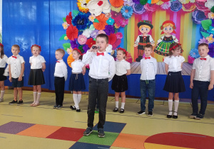Tymofii recytuje wiersz, w tle stoją dzieic ubrane na biało- granatowo