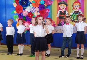 Zuzia recytuje wiersz, w tle stoją dzieic ubrane na biało- granatowo