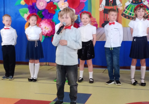 Denis recytuje wiersz, w tle stoją dzieic ubrane na biało- granatowo