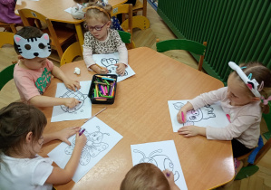 Dzieci przy zielonym stoliku kolorują kolorowanki zwierząt