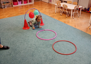 Dziewczynka w zielonej bluzie pokonuje tor przeszkód na niebieskim dywanie – z zaangażowaniem i radością uczestniczy w aktywności ruchowej