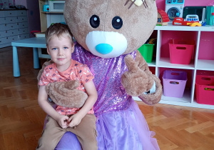 Janek ozuje do zdjęcia z misiem ubranym w fioletową spódniczkę i kokardkę