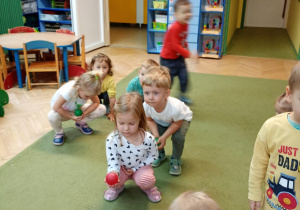 Dzieci starają się kucnąć tak, aby nie upuścić piłeczki na dłoni