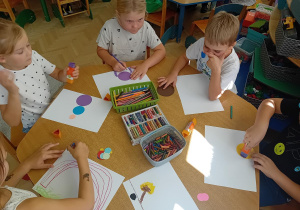Dzieci z czerwonego stolika tworzą pracę z kropek