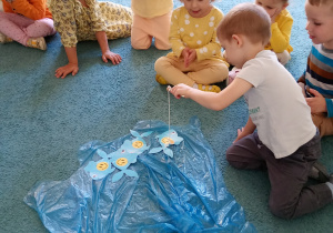 Chłopiec w białej koszulce stara się złowić rybkę, na której jest uśmiech.