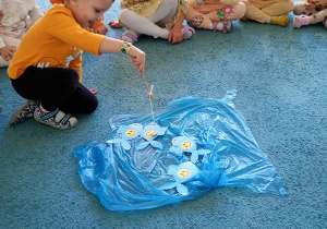 Chłopiec w żółtej bluzce łowi rybki rozłożone na niebsiekim dywanie.