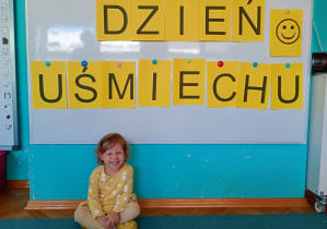 Dziewczyna w żółtej bluzce w białe kropki na tle npisu dzień uśmeichu przywieszonego na białej tablicy