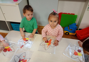 Nela i Mateusz siedzą przy stoliku. Przed sobą maja folię z konturem liścia.