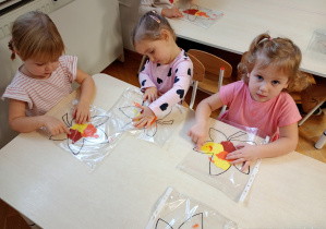 Dzieci siedzą przy stoliku. Na stolikach lezą folie z farbami i konturami liścia. dzieci rozporwadzaja paluszkiem farby, maluja liście.
