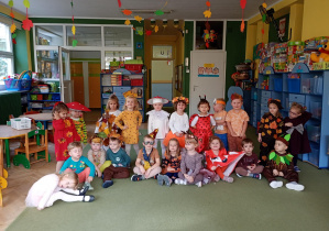 Dzieci prezentują swoje jesienne stroje na zdjęciu grupowym w sali