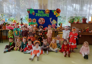 Dzieci prezentują swoje jesienne stroje na zdjęciu grupowym w szatni