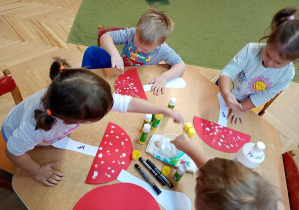 Dzieci palcami umoczonymi w białej farbie tworzą kropki na kapeluszu muchomora