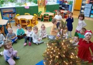 Dzieci obserwują choinkę przystrojoną w światełka