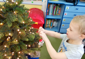 Chłopiec zawiesza na choince ozdobę przyniesioną z domu
