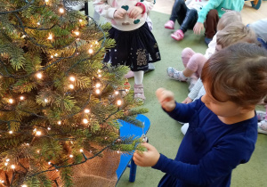 Dziewczynka zawiesza na choince ozdobę przyniesioną z domu