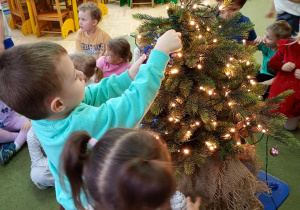 Dzieci zawieszają na choince ozdoby przyniesione z domu
