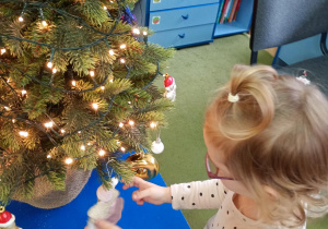Dziewczynka zawiesza na choince ozdobę przyniesioną z domu