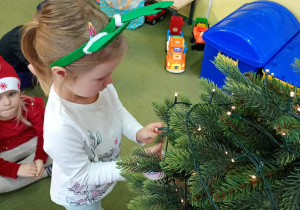 Dziewczynka zawiesza na choince ozdobę przyniesioną z domu