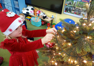 Dziewczynka zawiesza na choince ozdobę przyniesioną z domu