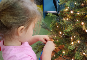 Dziewczynka zawiesza na choince ozdobę przyniesioną z domu