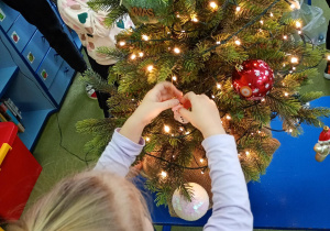 Dziewczynka zawiesza na choince ozdobę przyniesioną z domu