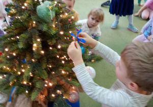 Chłopiec zawiesza na choince ozdobę przyniesioną z domu
