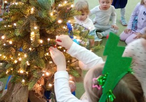 Dziewczynka zawiesza na choince ozdobę przyniesioną z domu