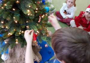 Chłopiec zawiesza na choince ozdobę przyniesioną z domu