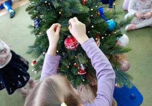Dziewczynka zawiesza na choince bombkę przyniesioną z domu