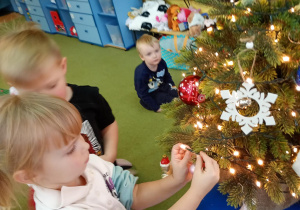 Dziewczynka zawiesza na choince ozdobę przyniesioną z domu