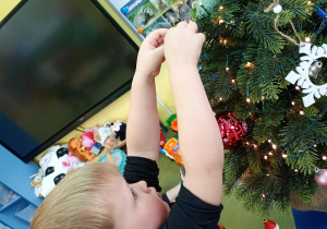 Chłopiec zawiesza na choince ozdobę przyniesioną z domu