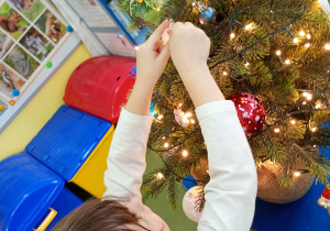 Dziewczynka zawiesza na choince ozdobę przyniesioną z domu