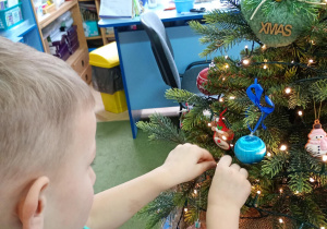 Chłopiec zawiesza na choince ozdobę przyniesioną z domu