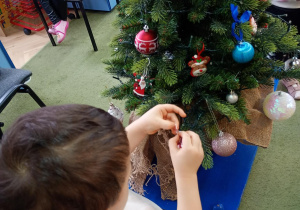 Chłopiec zawiesza na choince bombkę