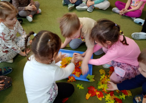 Dzieci zagrzebują figurkę jeża w liściach