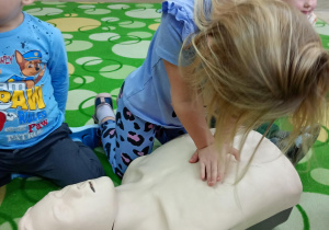 Dziewczynka uczy się wykonywać masaż serca na fantomie