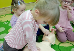 Dziewczynka uczy się wykonywać masaż serca na fantomie